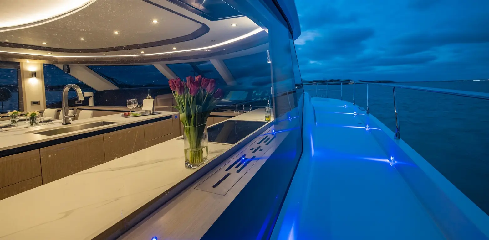Elegant yacht interior featuring a modern kitchen, illuminated by soft lighting, with a view of the sea at dusk.